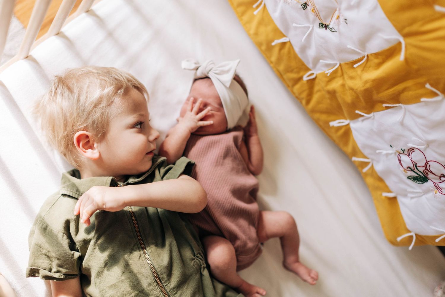 Two children lying on a bed with yellow and white floral bedding.