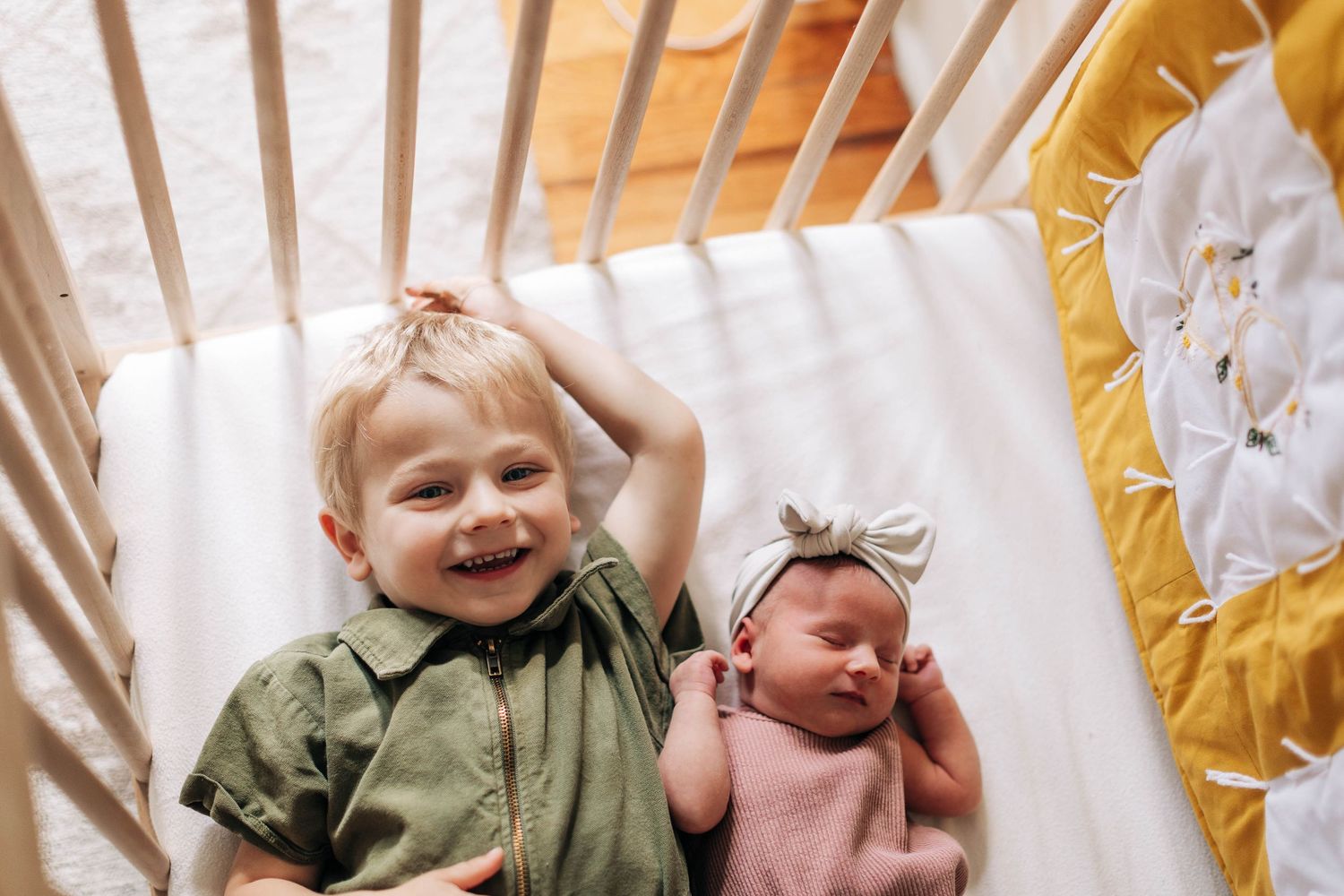 Two siblings share a sweet moment together on a crib mattress with yellow accents.