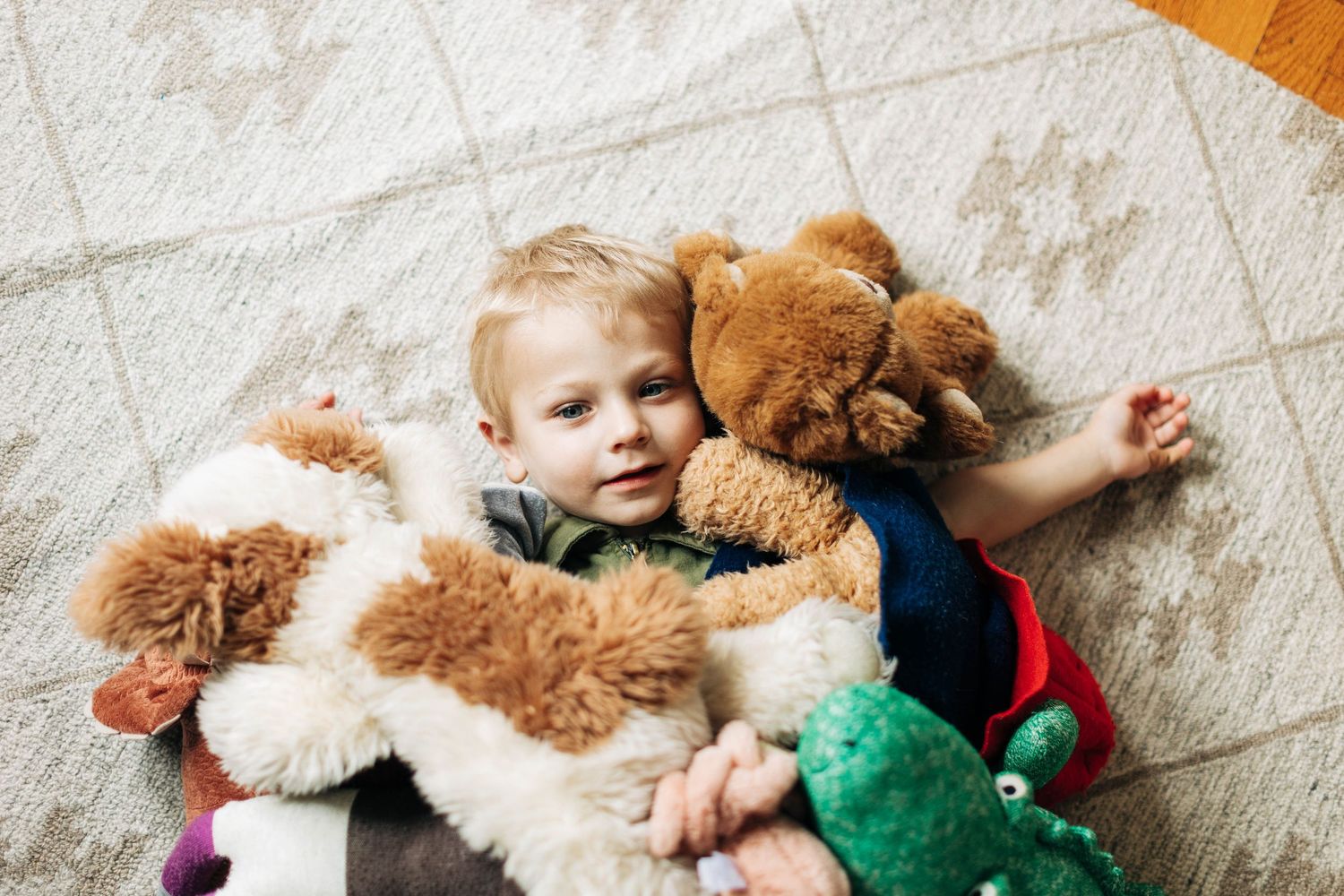 Child lying on carpet surrounded by plush stuffed animals.