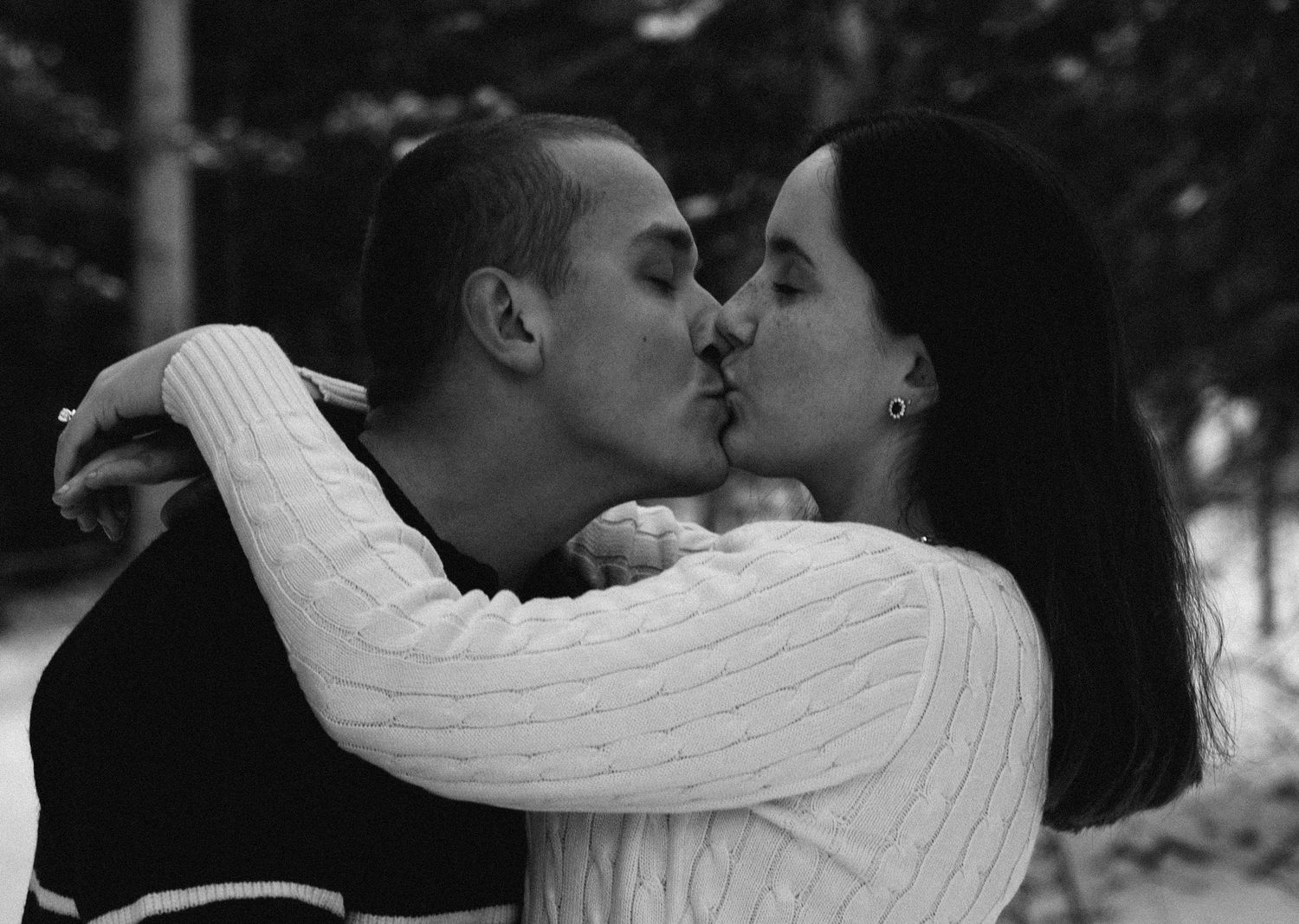 A romantic black and white photo of a couple sharing a kiss in winter, with the woman wearing a white sweater.