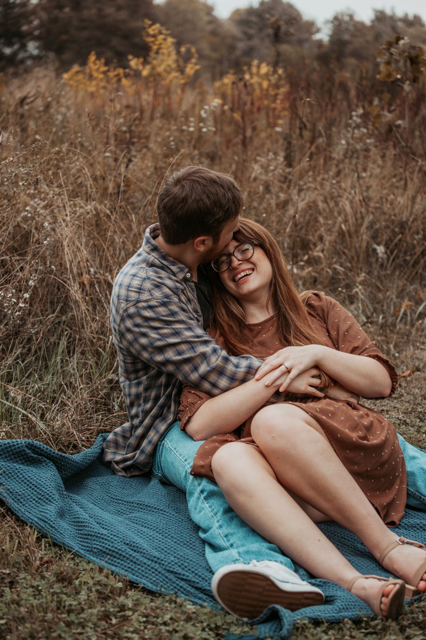 A couple shares an intimate moment while sitting on a blanket in a field of tall grass.