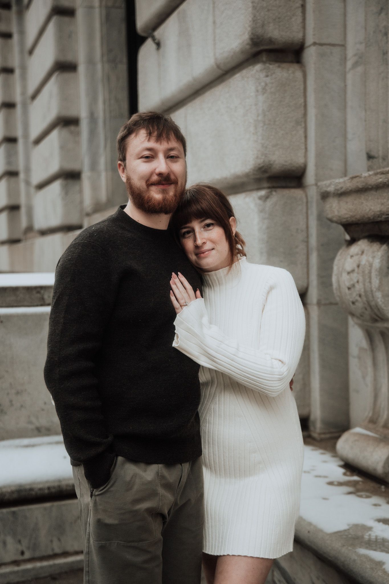 Romantic couple embracing against stone building exterior in winter.