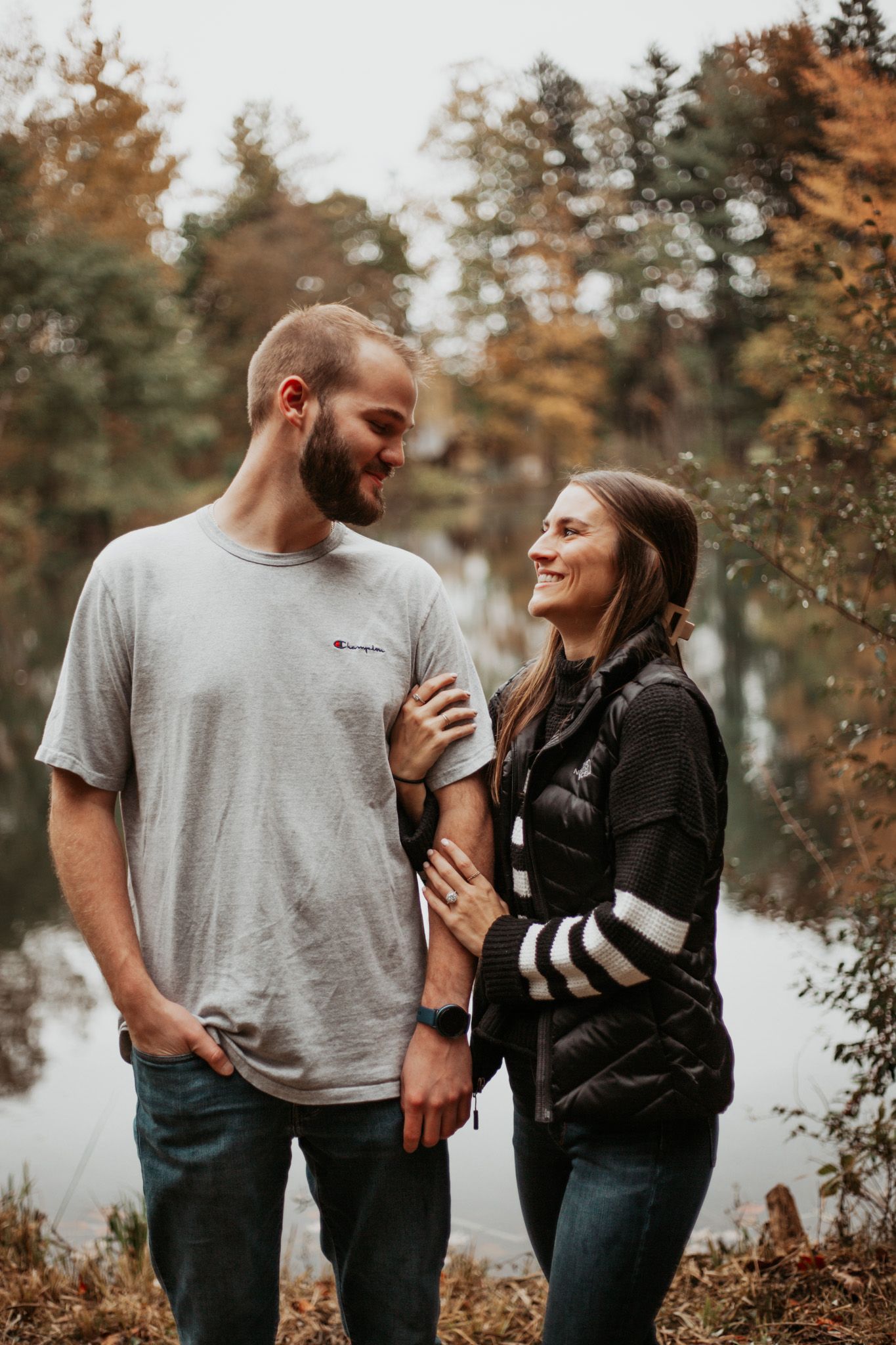 A couple shares playful moments together in a wooded setting during autumn.