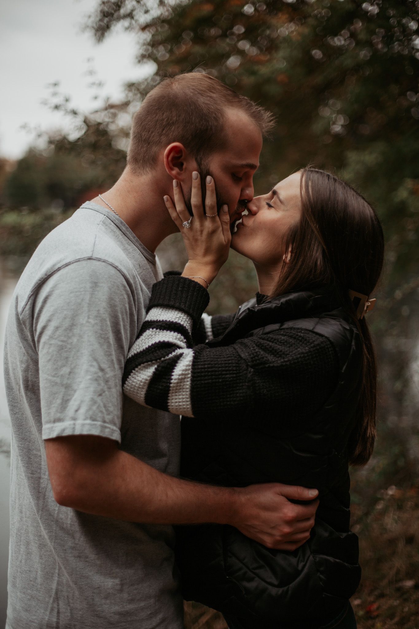 A romantic couple embraces and kisses in a moody outdoor setting.