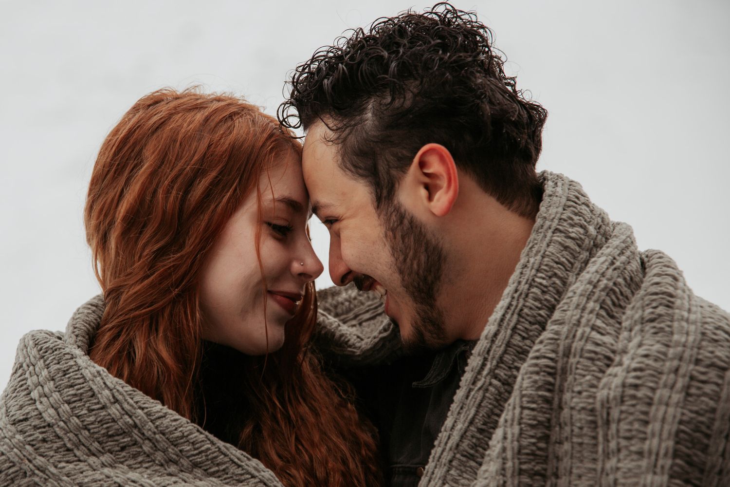 Intimate close-up of couple wrapped in knit blanket sharing tender moment.