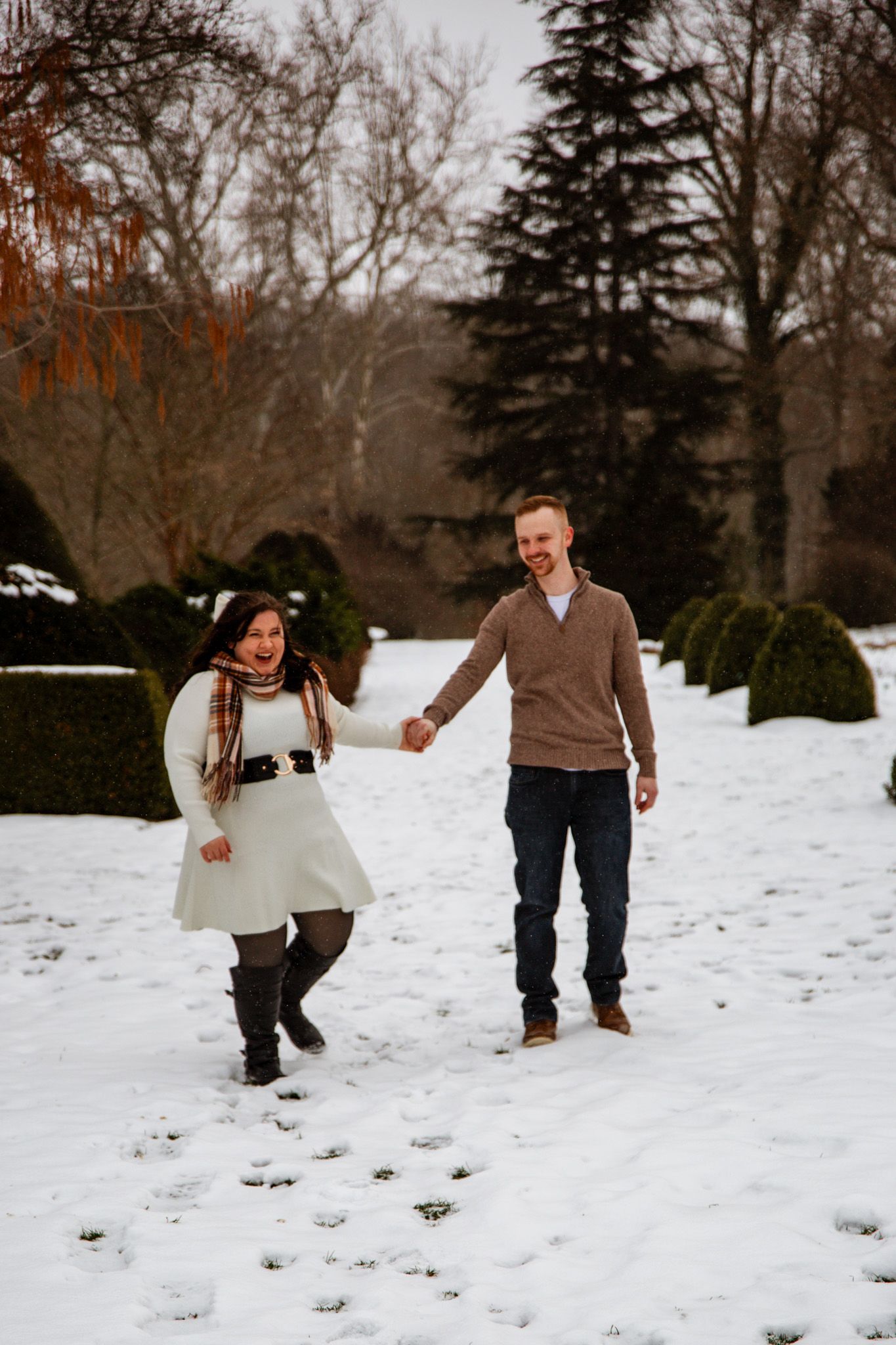 Couple holding hands while walking through snowy winter garden path.