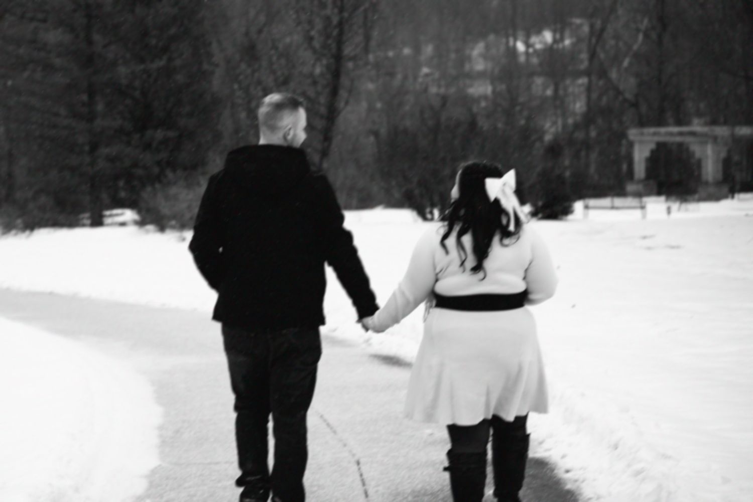 A couple walks hand in hand through a snowy winter landscape in black and white.