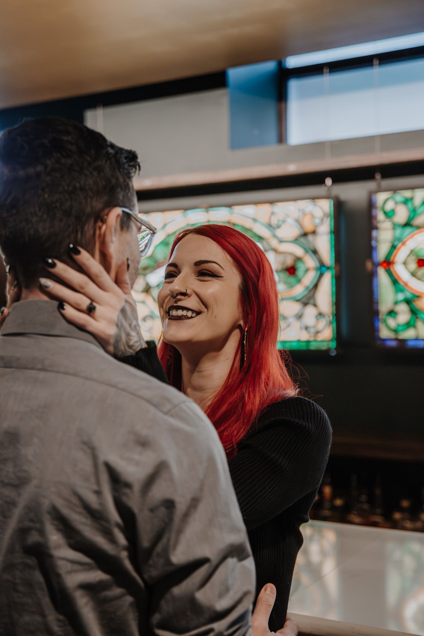 A couple shares an intimate moment in front of colorful stained glass windows.