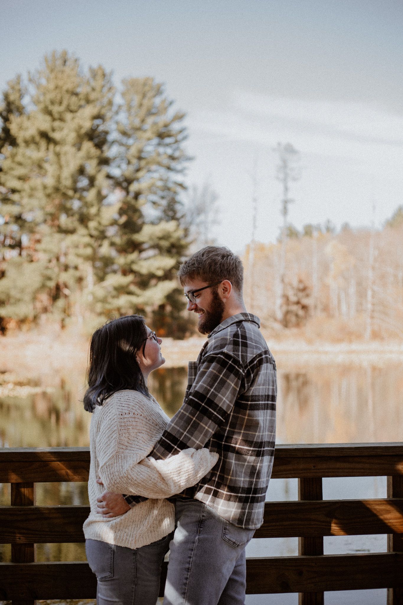 A couple shares a tender moment on a wooden deck overlooking a lake.