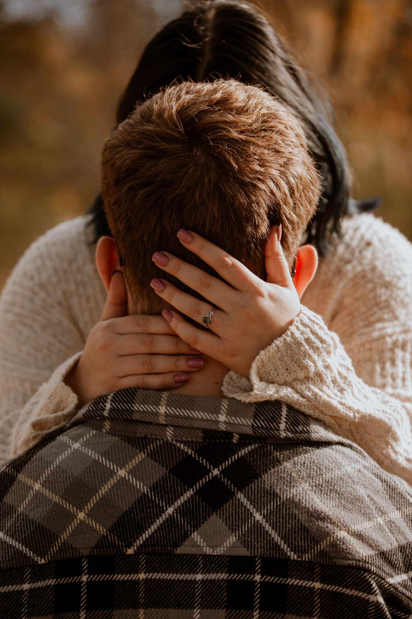 Close-up of hands tenderly embracing against a plaid jacket in golden light.