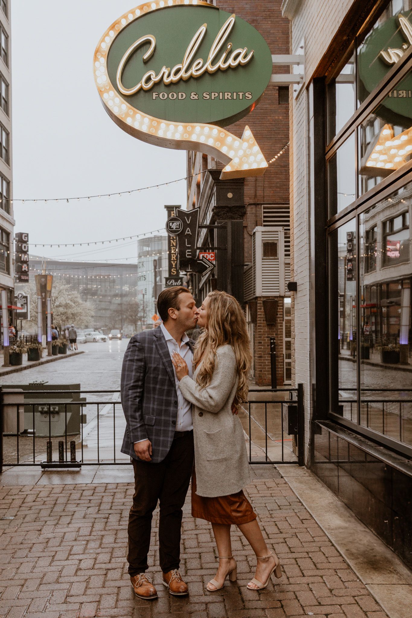 A couple shares romantic moments outside a vintage storefront with illuminated signage.