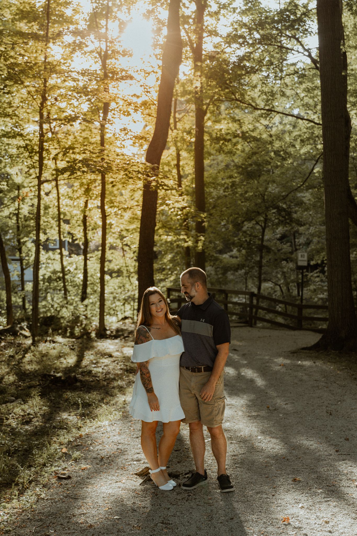 A couple walks together on a sunlit forest path during golden hour.