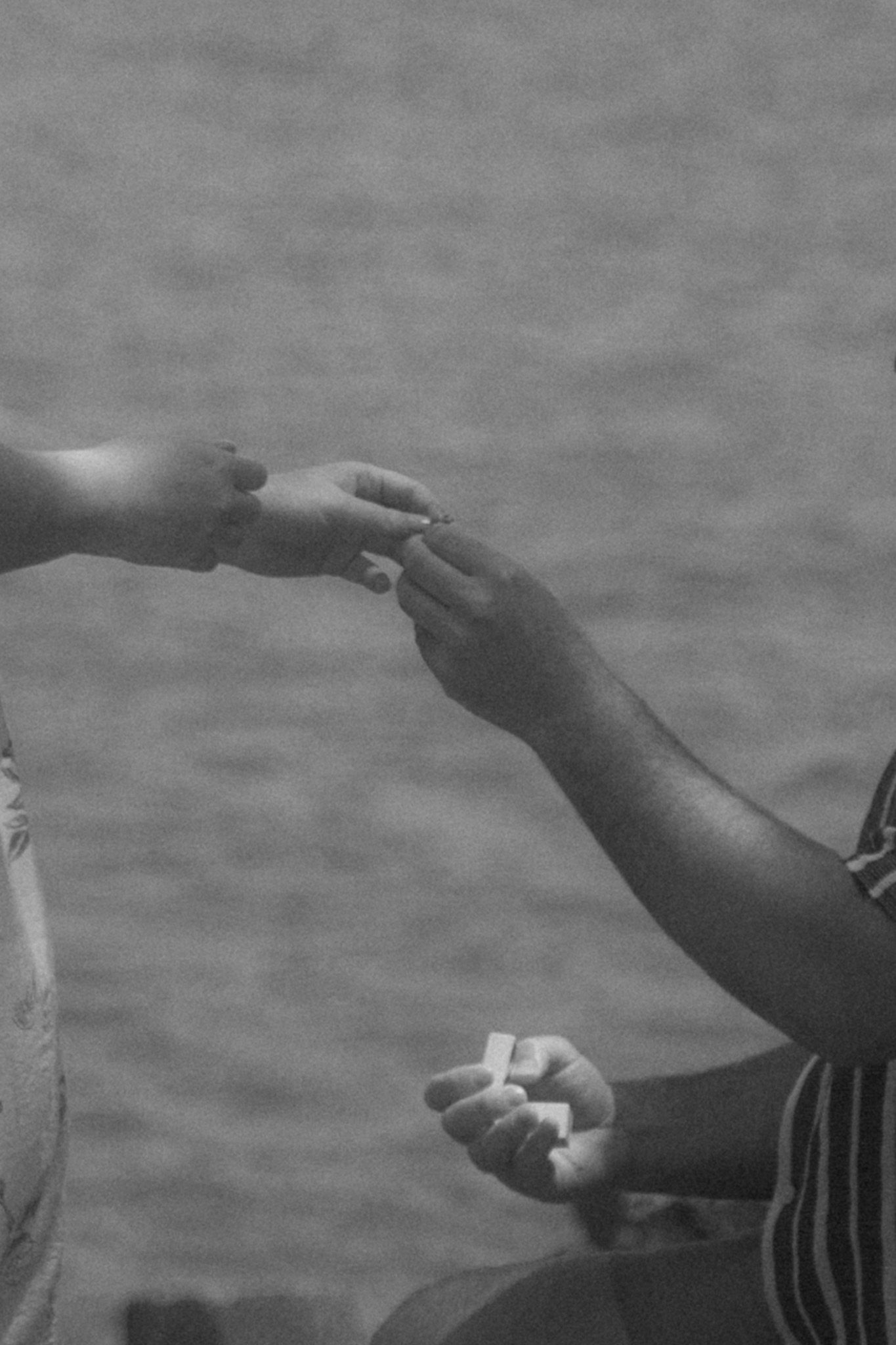 Close-up shot of hands exchanging something over water.
