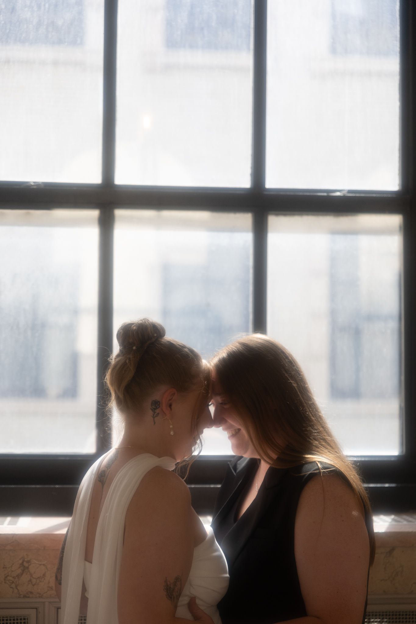 Silhouetted figures in tender moment against bright window background.