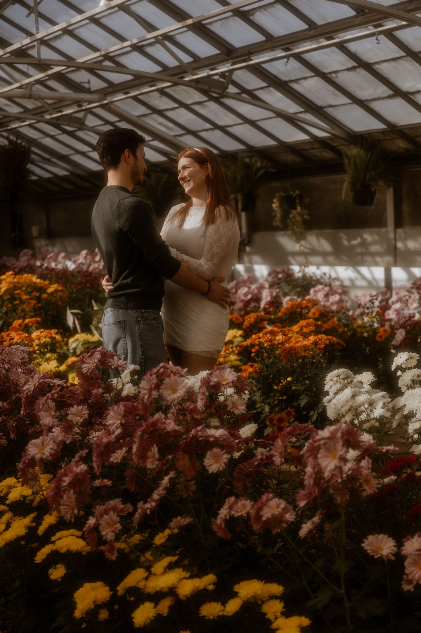 Couple browses colorful flower greenhouse filled with yellow and pink blooms.