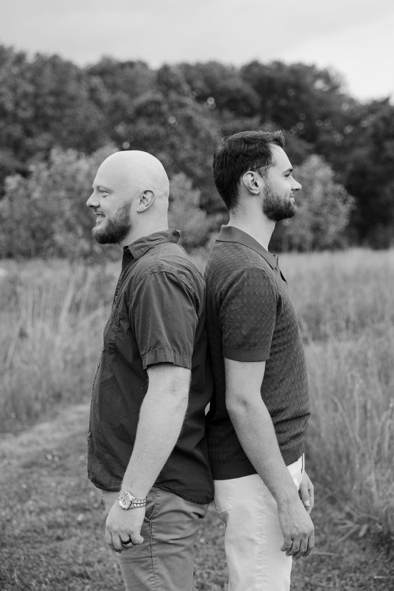 Two bearded men standing back-to-back in a field, black and white portrait photo outdoors.