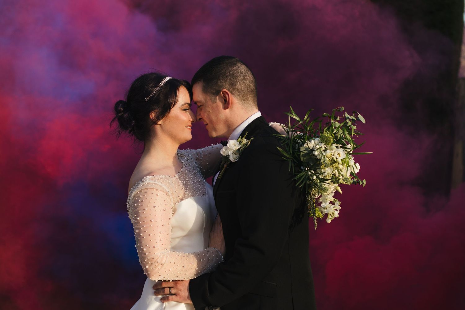 Romantic wedding portrait with dramatic red and purple smoke effects in background.