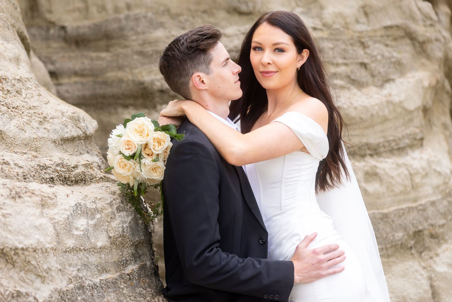 A romantic wedding portrait against a rocky cliff backdrop with a white bouquet.