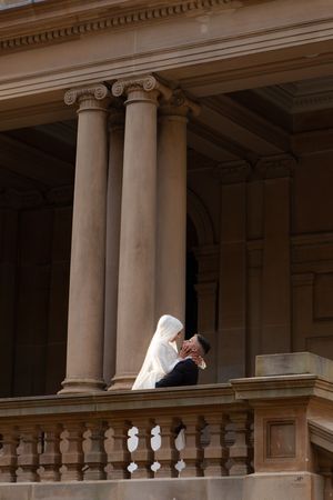 Muslim bride and groom share intimate moment on balcony flanked by classical stone columns.