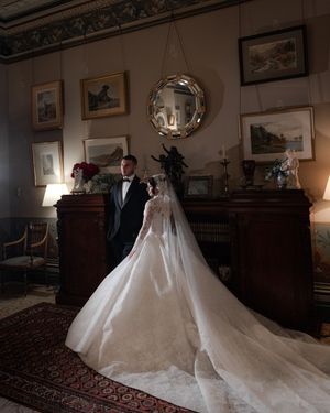 Bride and groom pose in an elegant antique-filled room, her cathedral train spread across a Persian rug.