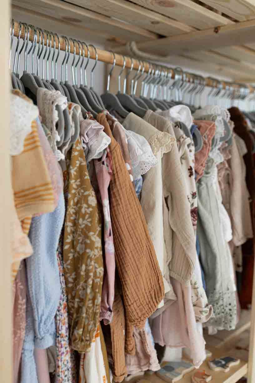 A clothing rack displays a collection of delicate baby dresses and children's clothing in soft pastel colors.