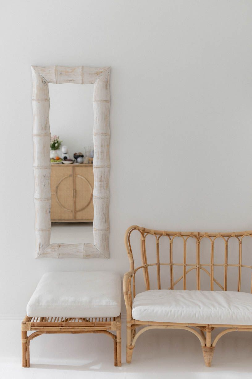 Minimalist interior with rattan furniture, white cushions, and a stone-framed mirror opening to a wooden cabinet.
