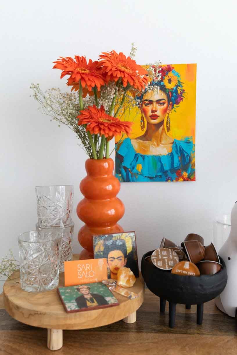 Modern interior decor setup featuring orange vases with red gerbera daisies and artistic wall prints in vibrant colors.