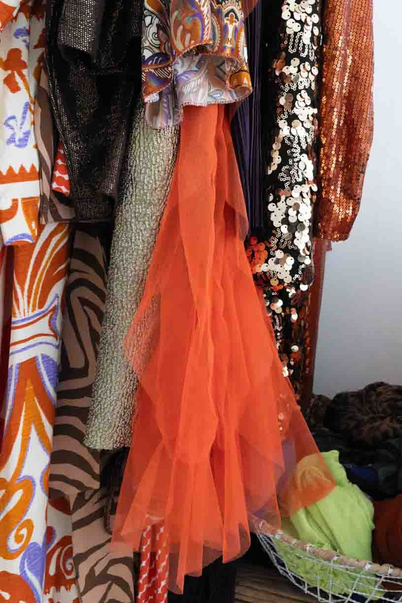 Orange tulle dresses with white and blue cheerleader uniforms hanging on display in a clothing store.