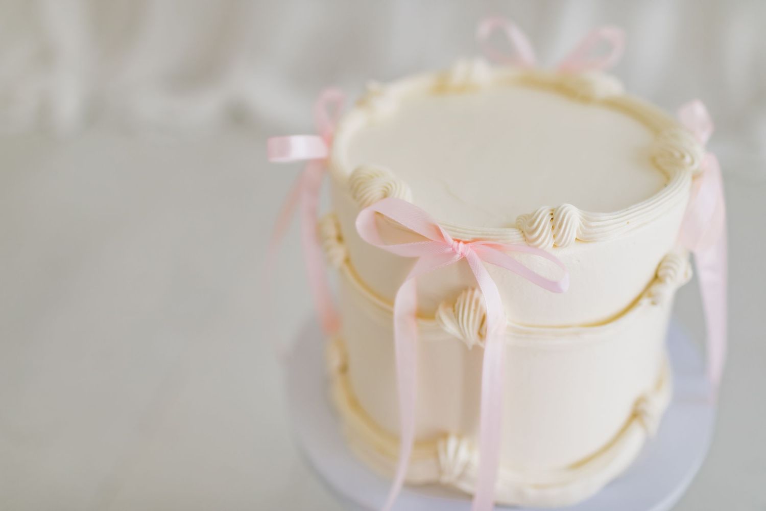 A close-up of a white wedding cake decorated with pink bows and intricate patterns.