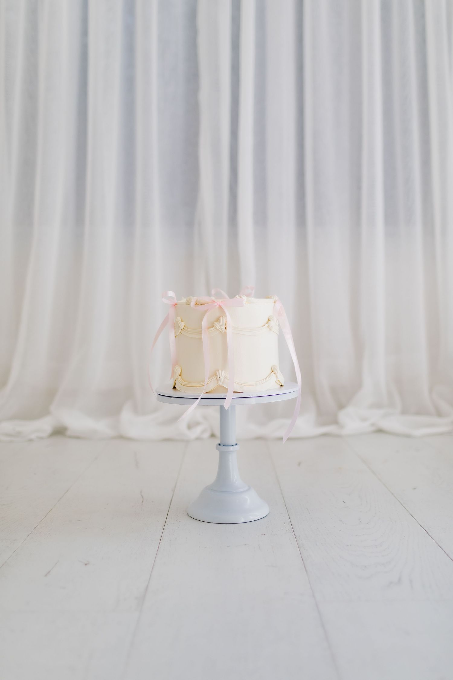 A simple white wedding cake on a pedestal against a light backdrop.