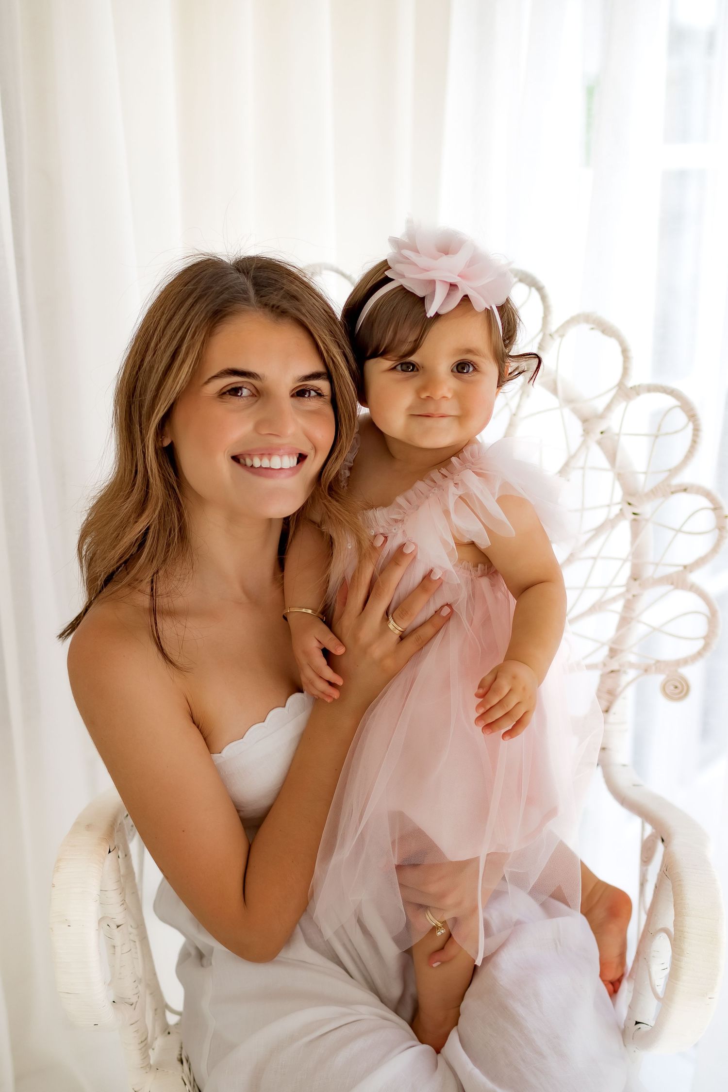 A joyful portrait of two people in coordinating white and pink outfits against white curtains.