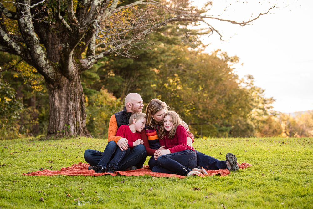Family snuggling together on the grass underneath a large tree