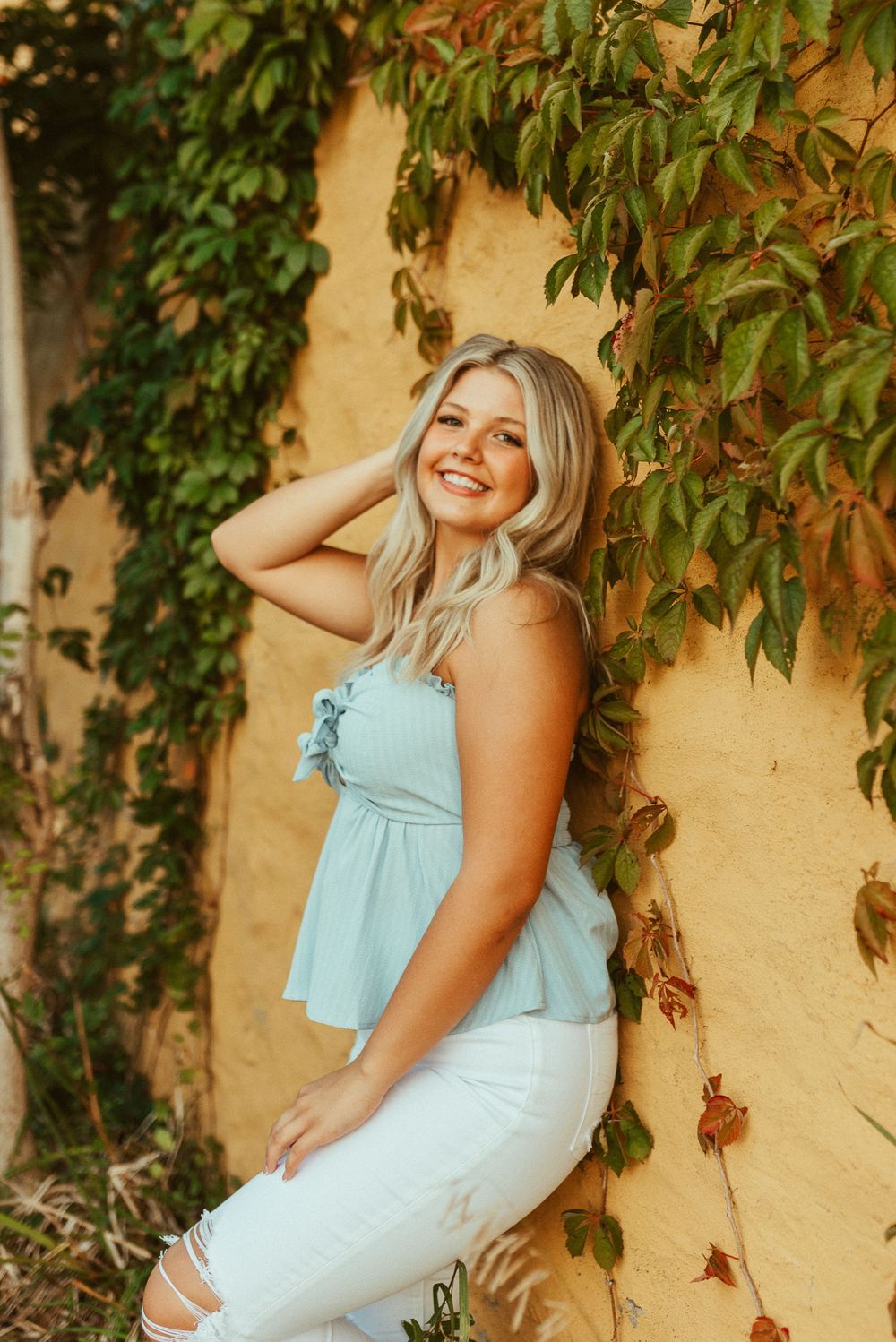 A casual portrait against a yellow wall with climbing vines creating natural framing.