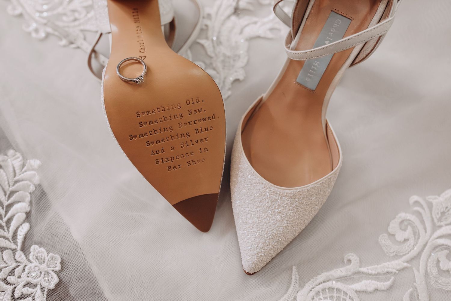 Elegant white bridal shoes with delicate details displayed on lace fabric.