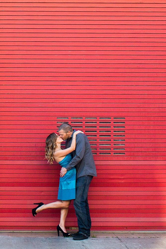 Romantic couple kissing against vibrant red wall with horizontal lines.