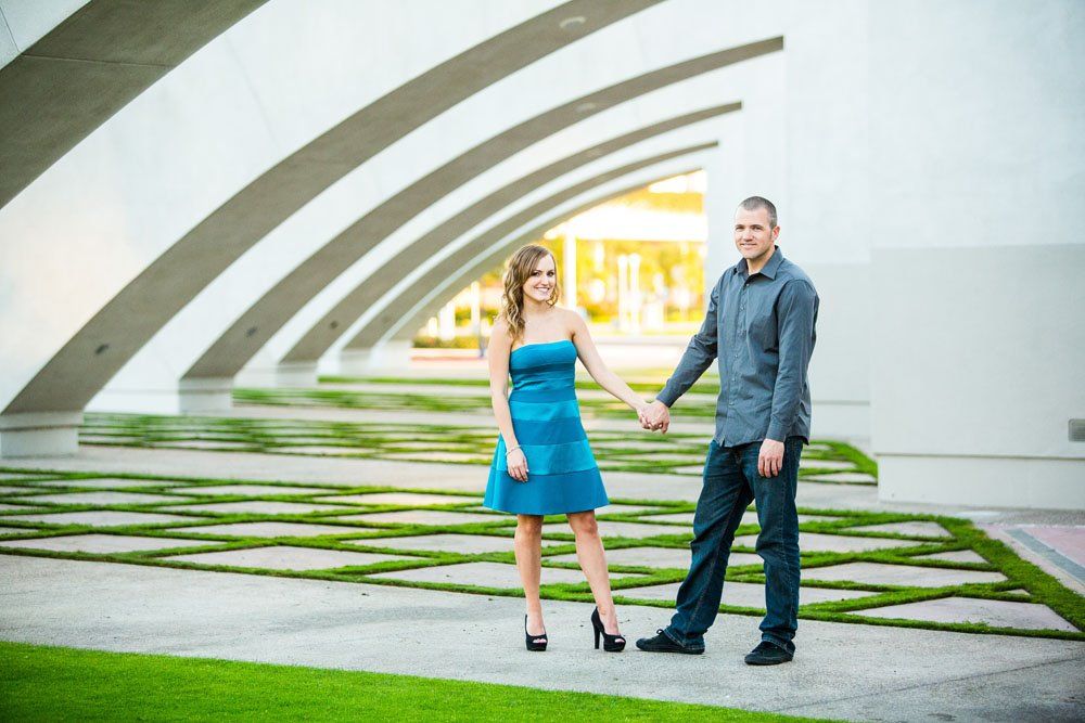 Couple holding hands under modern architectural arches with green reflective water.