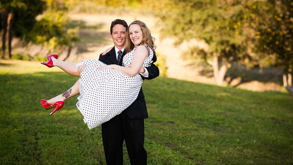 Man carrying woman in polka dot dress in park setting.
