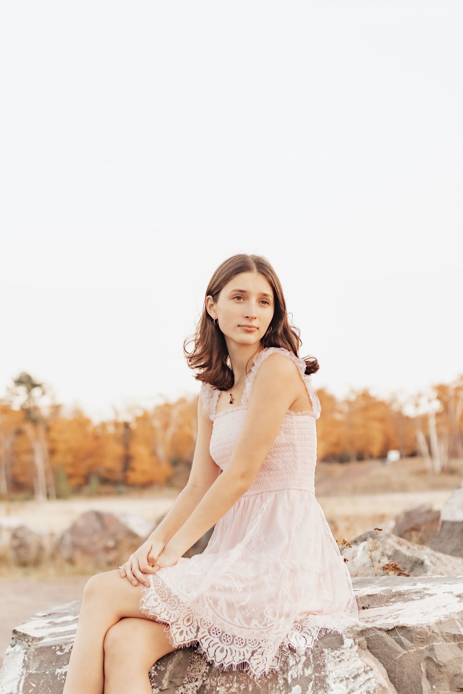A young woman in a dress poses on rocks during golden hour at sunset.