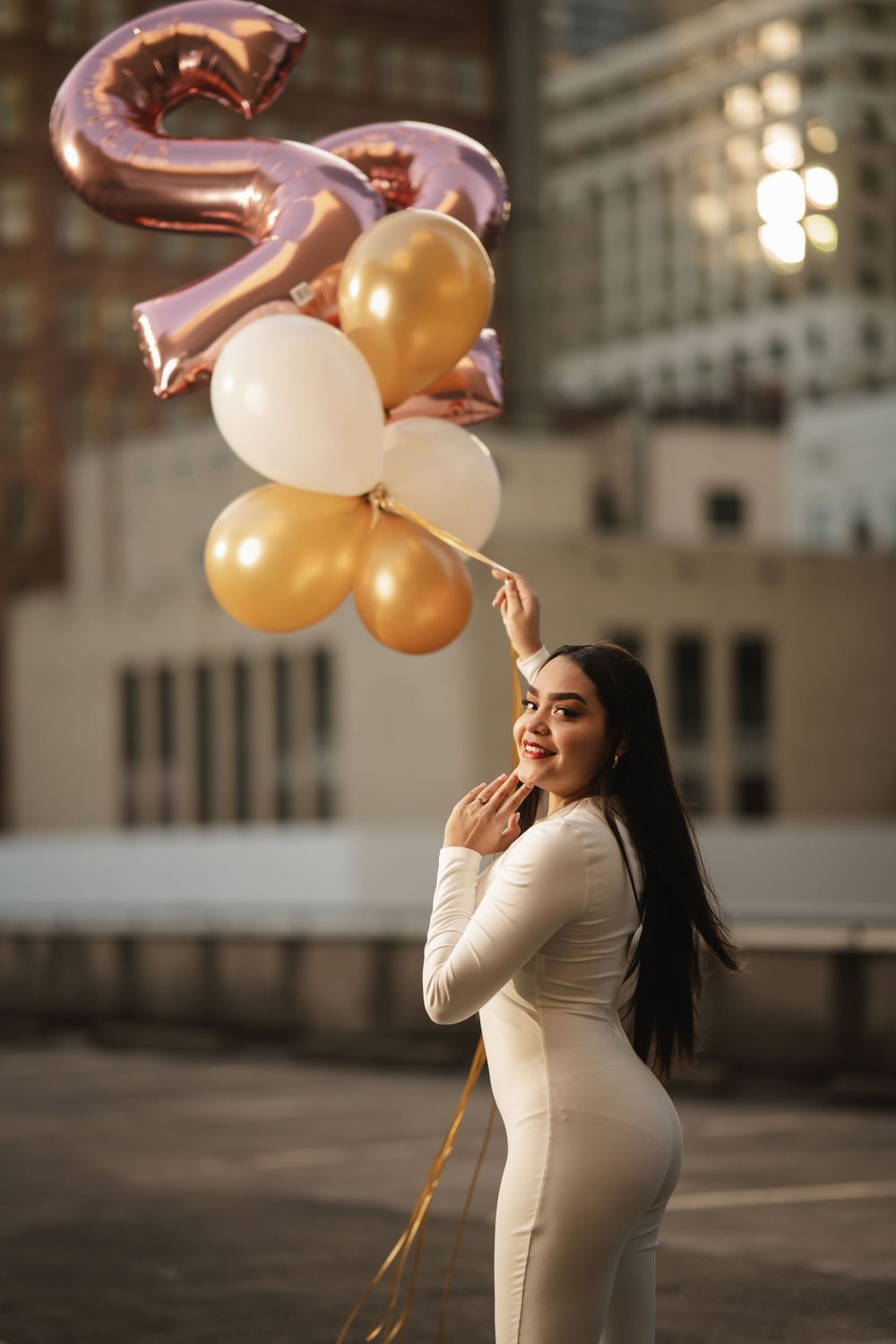 Elegant celebration scene with rose gold number balloons and golden party balloons against urban building backdrop.
