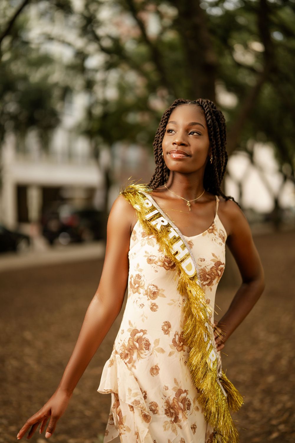 Elegant sleeveless dress with floral pattern and gold fringe detail photographed outdoors in natural lighting.