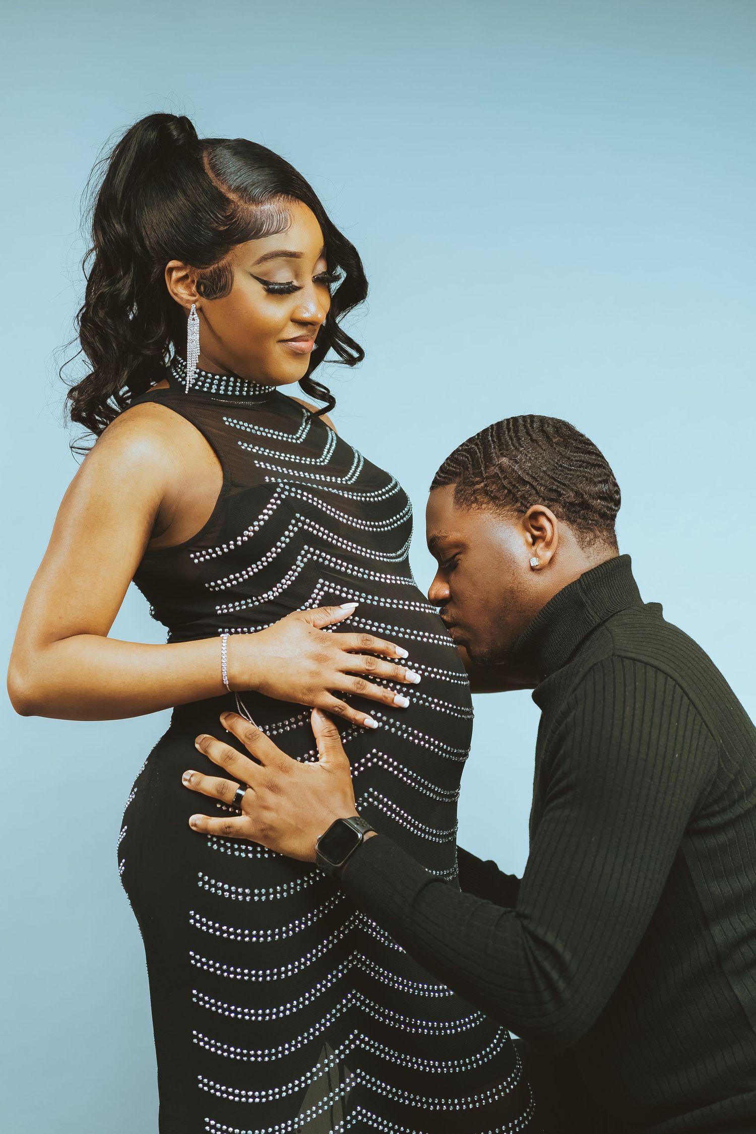 Intimate maternity portrait with couple in formal attire against blue backdrop.