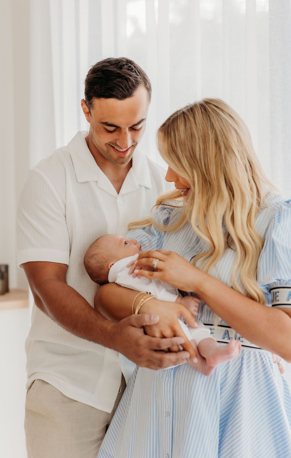 Baby, mum and dad cuddling together. Dad smiling down at baby. Family photography and newborn session.