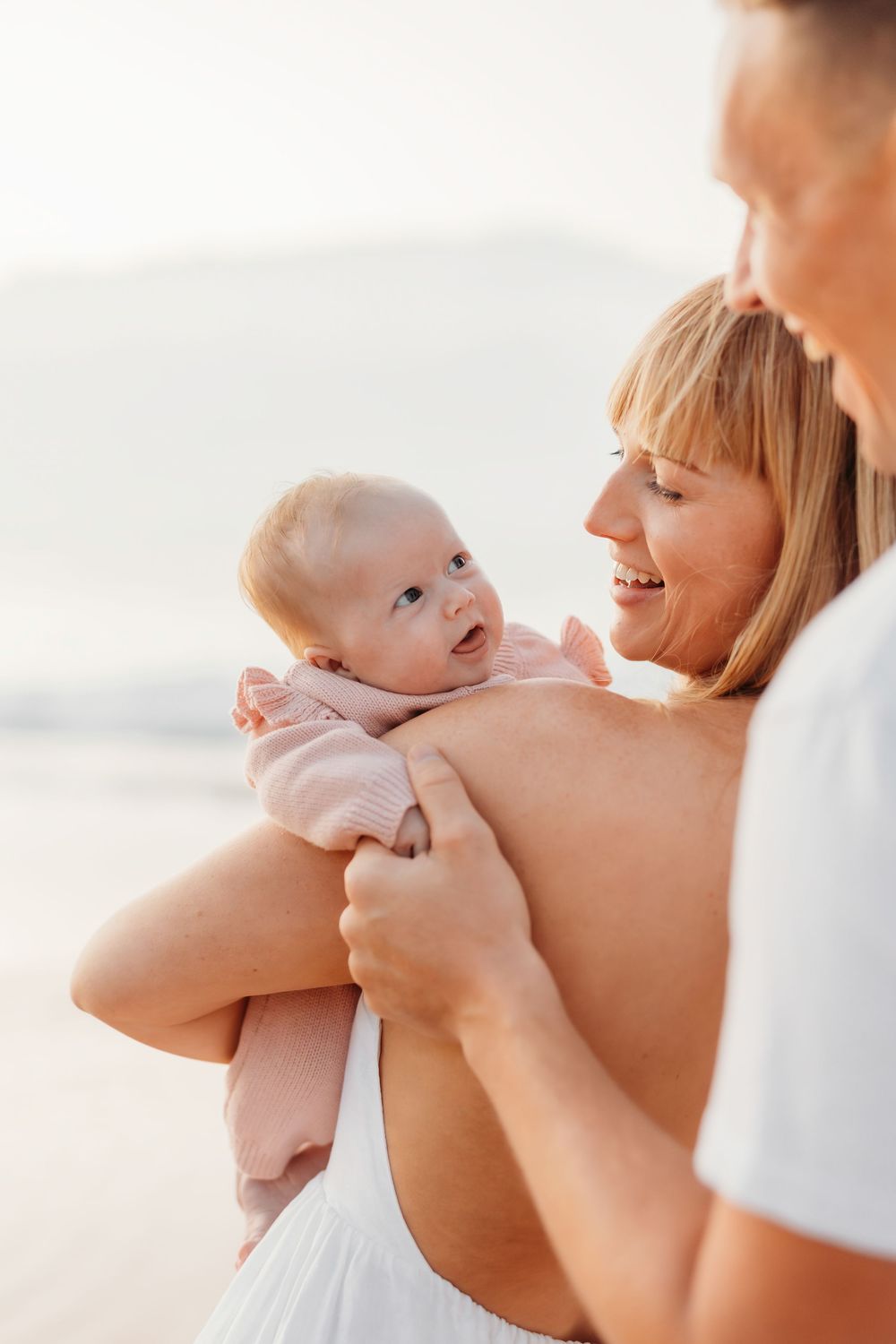 A mum and dad cuddling their newborn at the beach, taken by family photographer Charlotte Kate photography