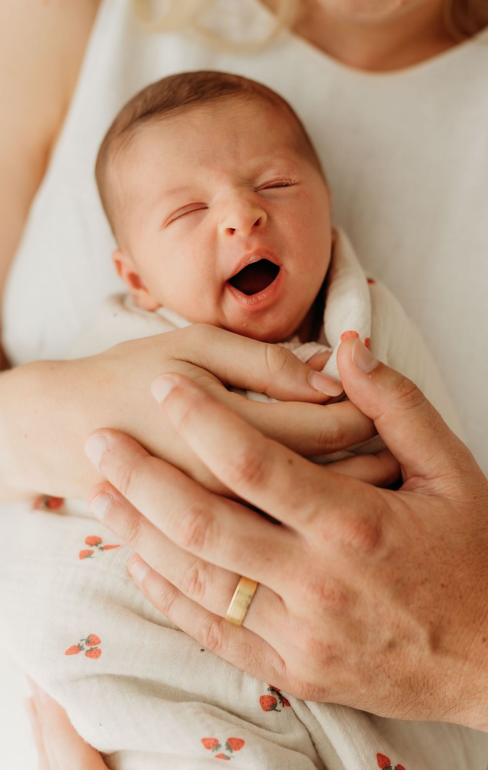 Cute baby yawning at the camera in dad's arms. Taken at home during their newborn session.