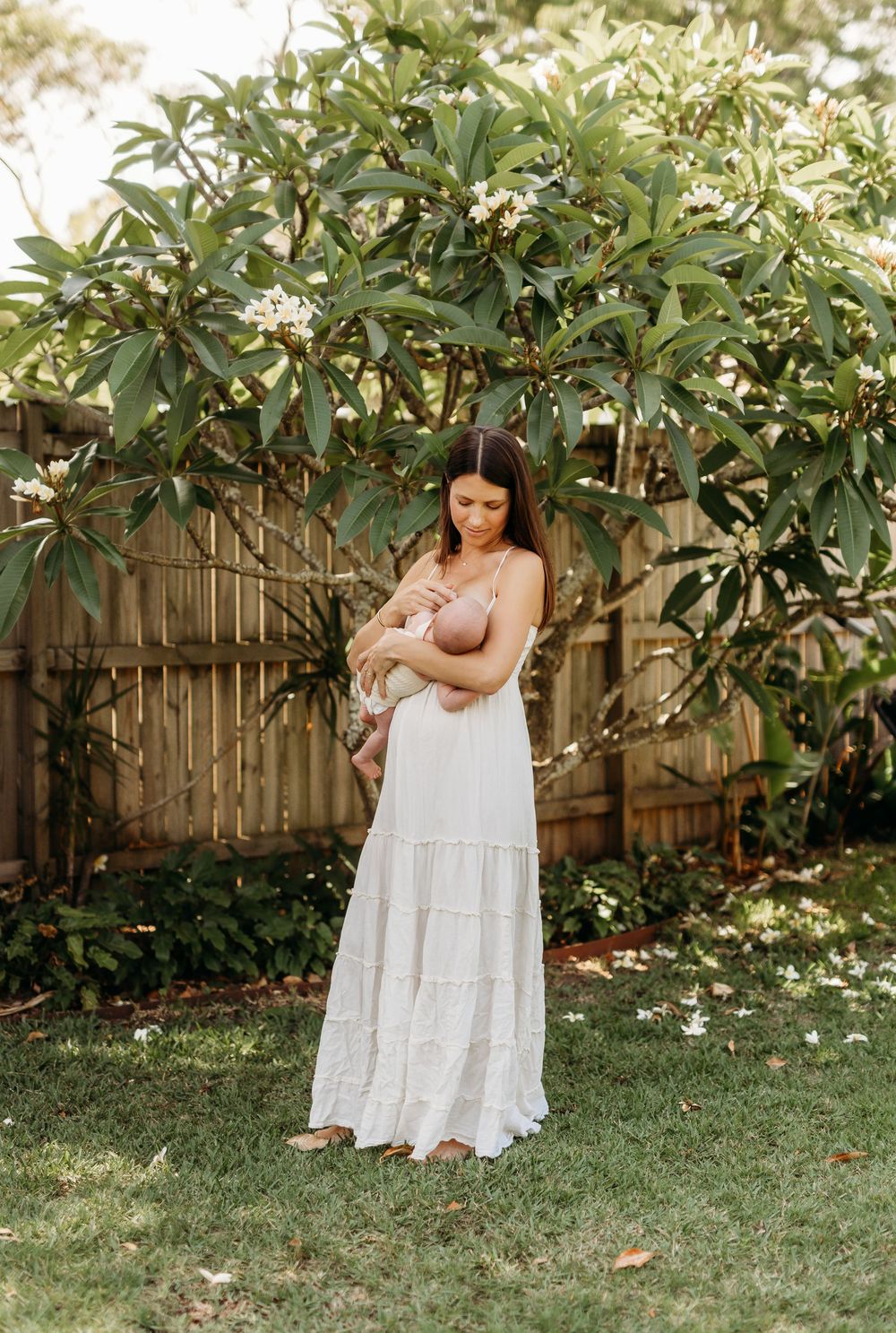 A portrait of a mum cuddling her baby in the green trees at home in their garden. Newborn photograher.