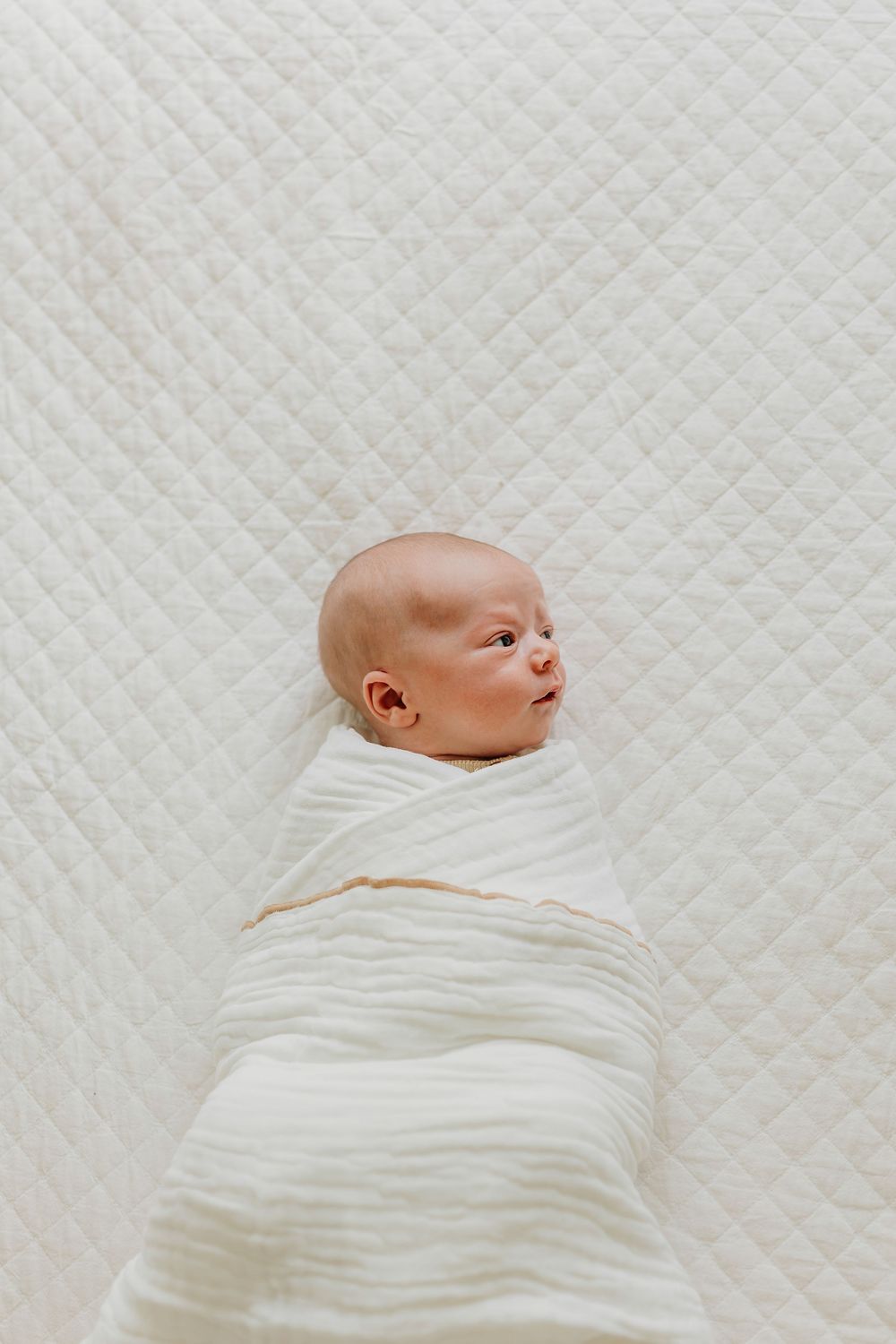 Newborn portrait taken at home, a baby laying on the bed wrapped in a white blanket. Newborn photographer.