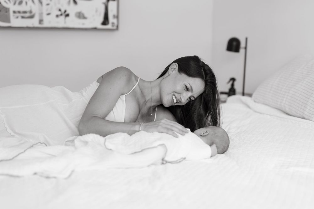 A mum cuddling her newborn on the bed at her home and smiling down at him. Newborn photography