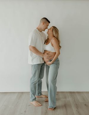 Casual indoor maternity photo of couple in white and denim sharing intimate moment at a studio in Huntington Beach