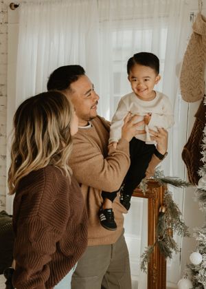Candid family moments captured against white brick wall with holiday greenery decor.