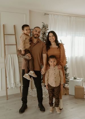 A family of four poses together in matching earth-toned outfits against a light interior background with decorative ladder.